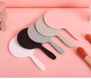 Close-up of portable mini handheld mirrors in five colors on a pink background