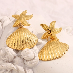 Detailed macro view of 18K gold starfish and seashell earrings on white textured stone