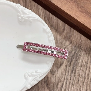 Detail view of rectangular silver hair clip with double-row pink rhinestones on ceramic plate