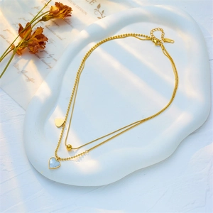 Gold double-layered necklace with heart shell pendant on a ceramic tray in natural light