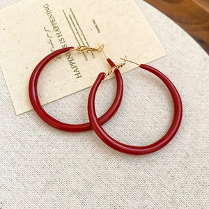 Macro shot of minimalist red enamel hoop earrings with gold metal needles on linen cloth