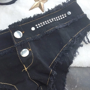 Detail der schwarzen Denim-Shorts mit Metallknöpfen, Strasssteinen und Fransensaum