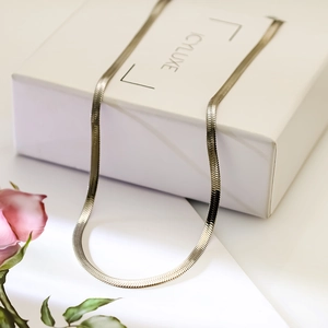 Detailed view of silver flat snake chain necklace draped over a white jewelry gift box