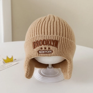 Dettaglio del ricamo Brooklyn sul berretto invernale in maglia beige con paraorecchie