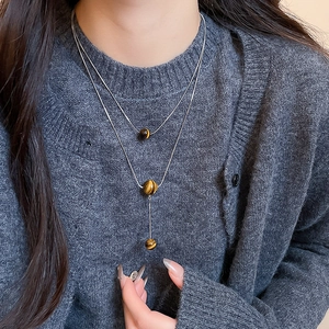 Detail of layered silver necklace featuring tiger eye stone beads on a knit sweater