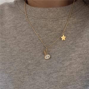Detail of gold beaded necklace featuring a white shell rabbit and star pendants worn over a sweater