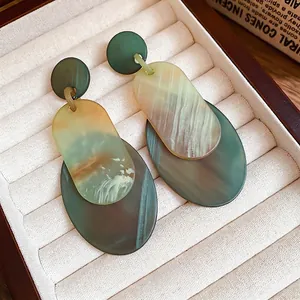Geometric acrylic drop earrings with green and yellow marble patterns in jewelry box