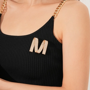 Close-up of sparkling rhinestone twisted letter M brooch on black knit sweater