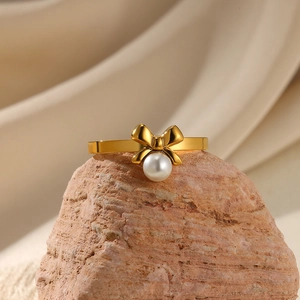 Detail of a golden bow ring with a white pearl on a rock with beige cloth background