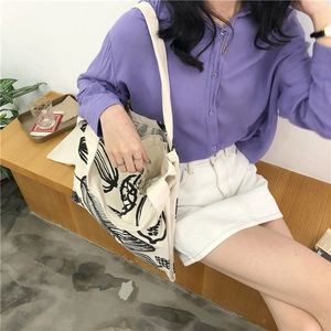 Lifestyle view of large ivory canvas tote bag with black leaf print on wooden bench