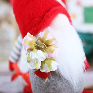 Detail of a plush Christmas gnome with red hat, white beard, and pink silk roses