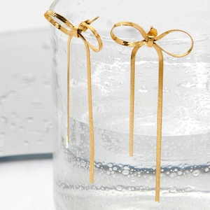 Golden stainless steel bow earrings with long tassel chain on a glass cup