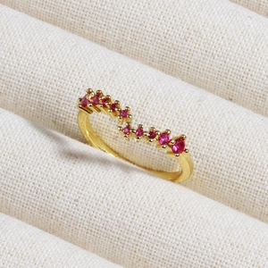 Close-up of gold wave ring with sparkling red gemstones on white fabric padding