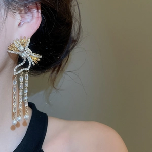 Detail of bow earrings with crystal tassels and white pearls worn by a model