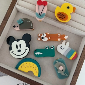 Detail shot of various acetate hair clips featuring animals and fruits in a wooden tray