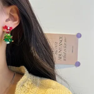 Close-up of beaded Christmas tree earrings with red ribbon bow and pearl on model