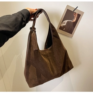 Detail of brown suede hobo bag with leather strap and tag against a minimalist wall