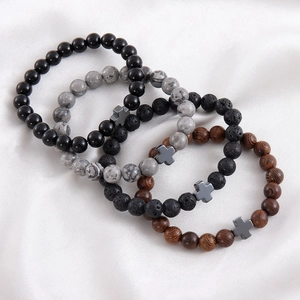 Detailed view of map stone and volcanic rock bracelets with metal crosses on white silk