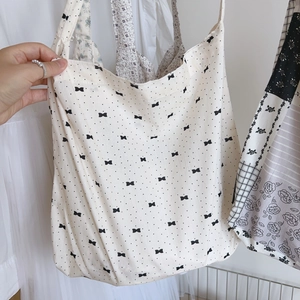 Détail d'un sac cabas en coton blanc souple orné de petits motifs de nœuds noirs