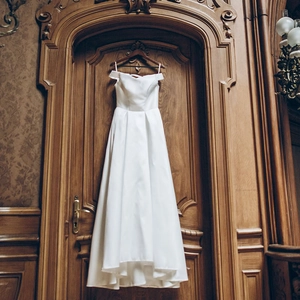 Elegant white satin off-shoulder wedding dress with a cinched waist and full flowing skirt