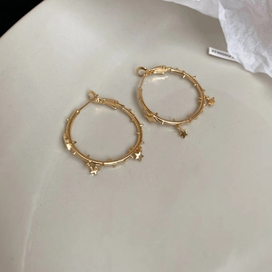 Macro shot of gold-plated hoop earrings featuring multiple star charms on a white surface