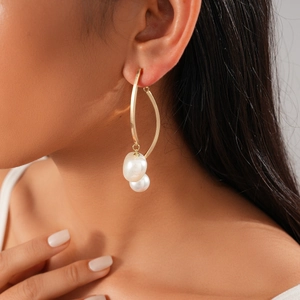 Gros plan de boucles d'oreilles dorées avec perles blanches portées par un modèle