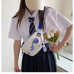 Detail of white canvas chest bag with blue straps, astronaut charm and decorative pins
