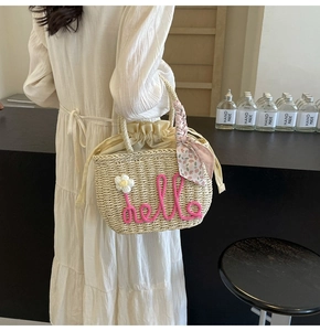 Detail of hand-woven straw bag with pink hello text and floral scarf detail