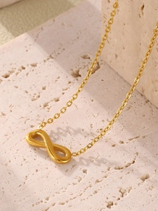 Détail du pendentif infini doré avec chaîne fine sur un support en pierre beige texturé