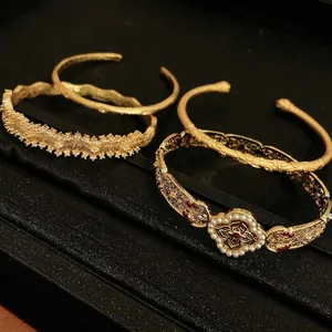 Elegant gold zircon bracelets with pearls and red gemstones on a black textured background