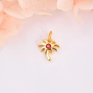 Gold palm tree pendant with red zircon stone centered on soft floral background