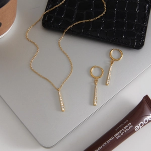 Détail d'un ensemble collier et boucles d'oreilles en acier doré et zircons sur laptop
