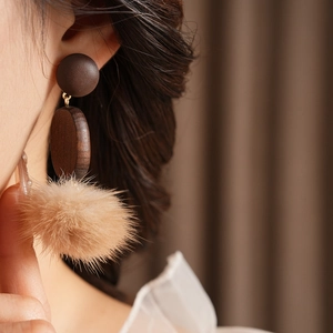 Close-up of wood and pompom earrings worn by a model in soft lighting