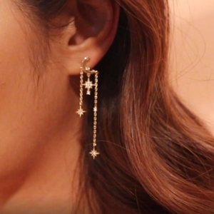 Detail of gold star and moon tassel earrings worn by a model with a soft bokeh effect