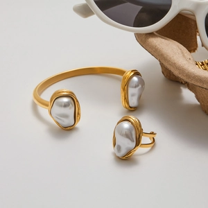 Vue détaillée d'un ensemble bracelet jonc en acier doré et bague perle sur fond blanc