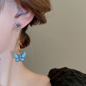 Close-up of elegant long butterfly earrings with blue enamel drop and silver flower studs