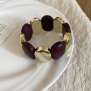 Detailed close-up of acrylic oval geometric link bracelet in gold and burgundy red