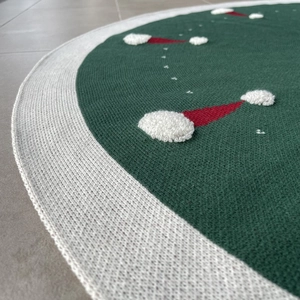 Détail du tapis de sapin de Noël en tricot vert avec motifs bonnets rouges et bordure blanche