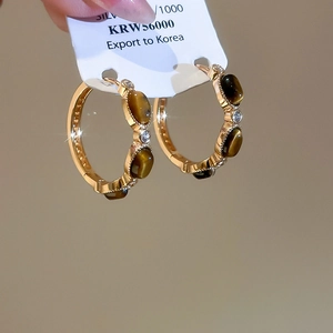 Close-up of gold plated earrings featuring oval tiger eye stone and zircon accents