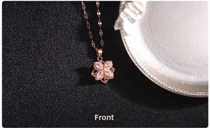 Close-up of a rose gold spinning clover necklace with zircons on a black textured background
