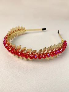 Detail of golden metal headband featuring leaf charms and multi-faceted red crystal beads