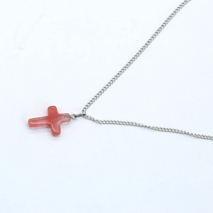 Cross necklace with red translucent stone pendant and silver chain on white background
