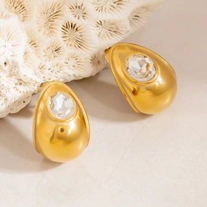 Close-up of golden teardrop earrings with sparkling crystal centers on coral background