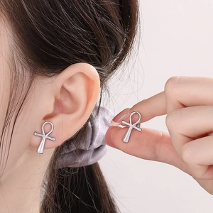 Macro view of silver stainless steel Ankh cross stud earrings worn on a model ear