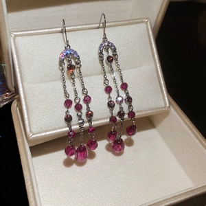 Vue détaillée des boucles d'oreilles pompons à trois rangs avec cristaux violets et magenta