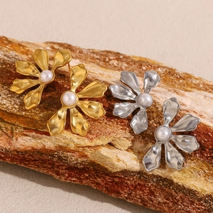 Macro shot of gold and silver flower stud earrings with pearls on rustic wood