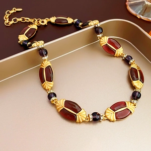 Vintage style gold necklace with deep red and purple gemstones on a golden tray