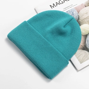 Detailed knit texture of a teal blue beanie hat displayed with a fashion magazine