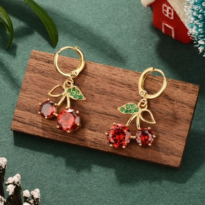 Close-up of gold cherry earrings with red and green zircons on a festive wood display