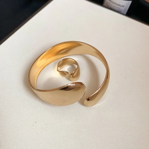 Polished gold cuff bracelet and matching ring set displayed on a white textured stand